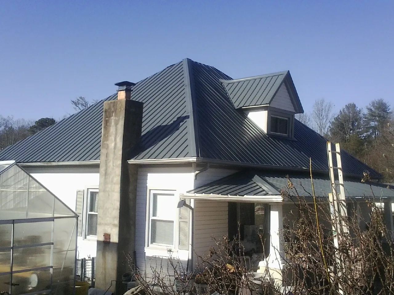 Dark blue standing seam metal roof on a white farmhouse with dormer — Slate & Tile Roof Repair by Roofing Brothers in Scottsmoor