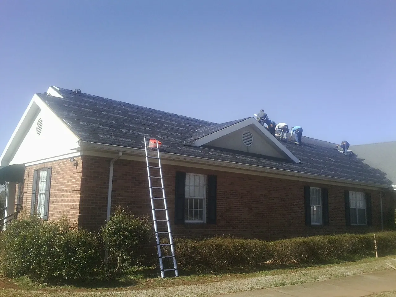 Crew tearing shingles off a brick ranch roof with a ladder set — Emergency Roof Repair work by our crew in Scottsmoor