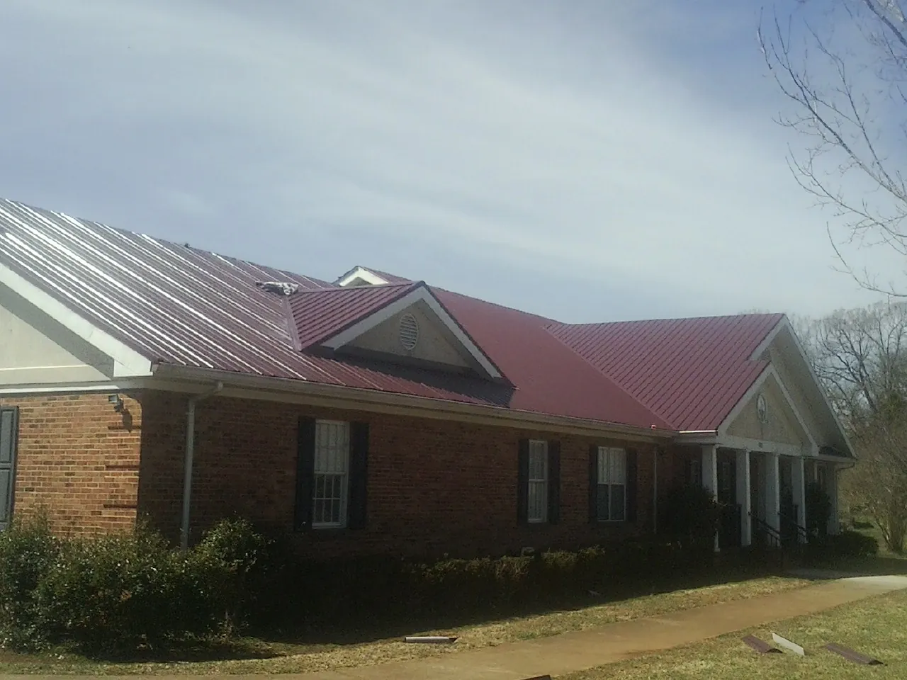 Red metal roof with gabled entries on a long brick building, from a Hail Damage Roof Repair job in Scottsmoor