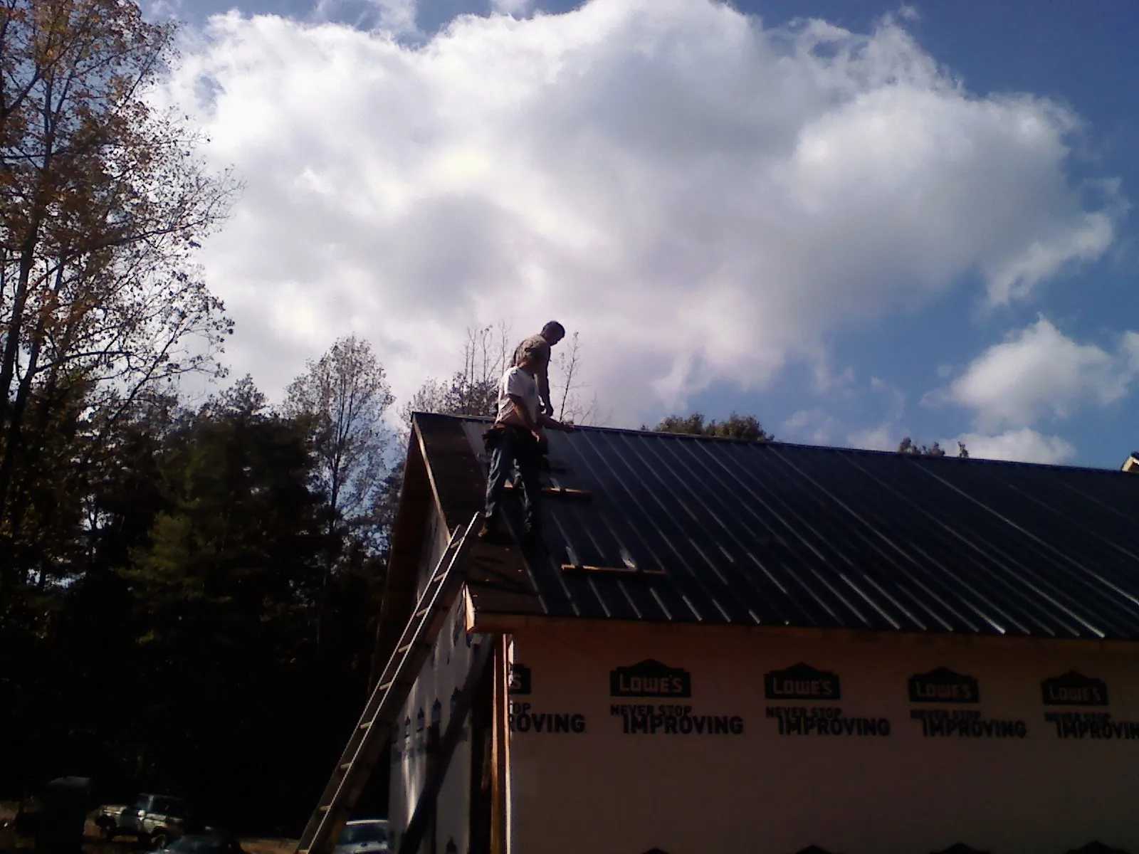 Roofer fastening dark metal panels high against a cloudy sky, from a Roof Inspection job in Scottsmoor