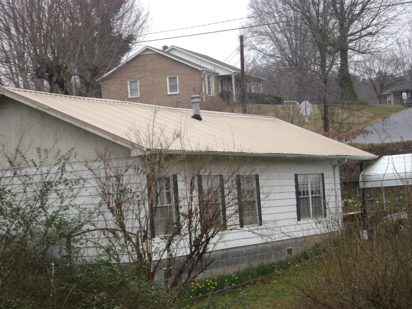 Tan metal roof on a white sided house set into a hillside — Commercial Roofing by Roofing Brothers in Scottsmoor