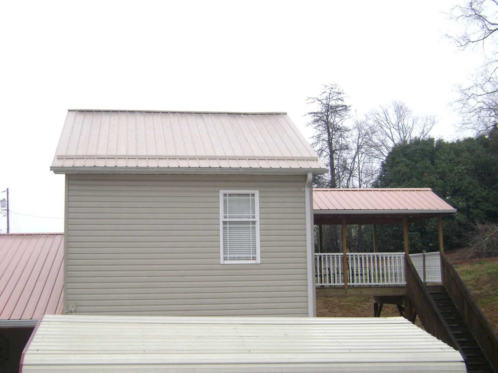 Tan metal roofs on a two story addition and attached porch, from a Roof Replacement job in Scottsmoor